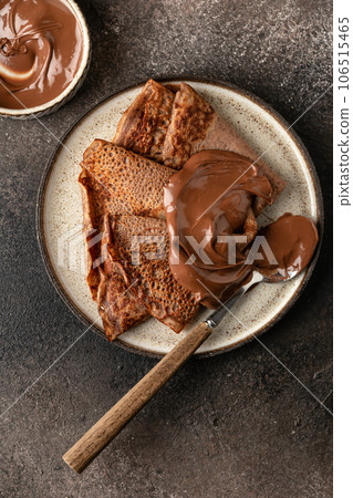 Chocolate crepes with chocolate paste on brown textured background rustic style top view, flat lay Chocolate crepes with chocolate paste on brown textured background rustic style top view, flat lay 106515465