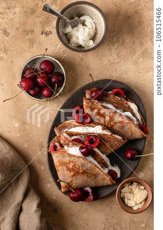 Chocolate crepes with cherry and whipped cream and almond petals on brown textured background rustic style top view, flat lay. Black forest recipe Chocolate crepes with cherry and whipped cream and almond petals on brown textured background rustic style top view, flat lay. Black forest recipe 106515466