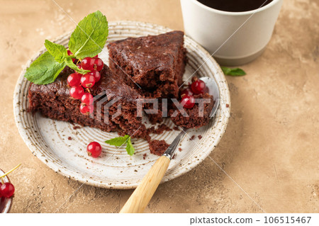 Two pieces of chocolate cake brownie close up decorated with red currant berries and mint for coffee on beige textured background 106515467