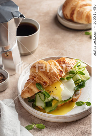 Croissant sandwich with fried egg, cheese, cucumber and micro greens and coffee over beige background. Healthy delicious breakfast Croissant sandwich with fried egg, cheese, cucumber and micro greens and coffee over beige background. Healthy delicious breakfast 106515486