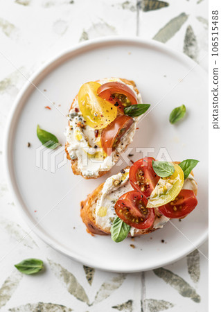 Bruschetta sandwiches with tomatoes, cream cheese, olive oil and basil on white plate on printed tile background close up, top view. Traditional italian antipasti Bruschetta sandwiches with tomatoes, cream cheese, olive oil and basil on white plate on printed tile background close up, top view. Traditional italian antipasti 106515488
