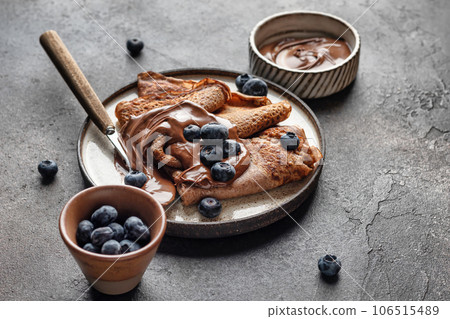 Chocolate crepes with blueberry and chocolate paste on brown textured background rustic style Chocolate crepes with blueberry and chocolate paste on brown textured background rustic style 106515489