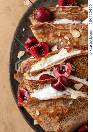 Chocolate crepes with cherry and whipped cream and almond petals on brown textured background close up top view, flat lay. Black forest recipe Chocolate crepes with cherry and whipped cream and almond petals on brown textured background close up top view, flat lay. Black forest recipe 106515499