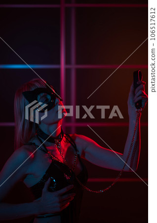 Blonde girl in a leather mask and handcuffs in the bedroom in red blue neon light. Role-playing games. Blonde girl in a leather mask and handcuffs in the bedroom in red blue neon light. Role-playing games. 106517612