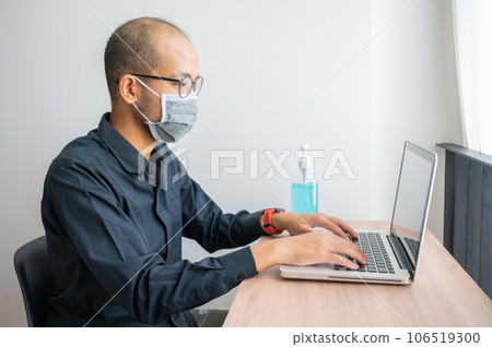 Portrait of young Asian businessman wearing mask while working at office with a bottle of hand sanitizer. Conceptual of new normal lifestyle during covid-19 pandemic. Portrait of young Asian businessman wearing mask while working at office with a bottle of hand sanitizer. Conceptual of new normal lifestyle during covid-19 pandemic. 106519300