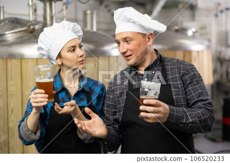 Woman and man brewmasters checking quality of beer and discussing Woman and man brewmasters checking quality of beer and discussing 106520233