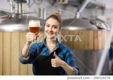 Female brewer showing thumbs up while holding glass of beer Female brewer showing thumbs up while holding glass of beer 106520276