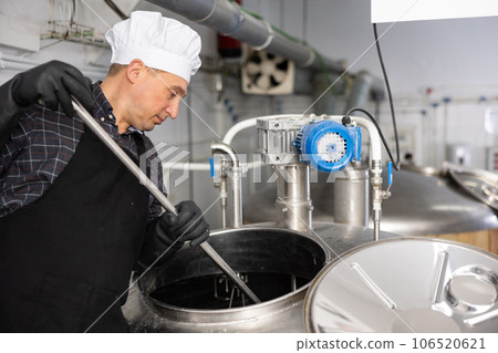 Brewery worker stirring raw materials in fermenter for beer production 106520621