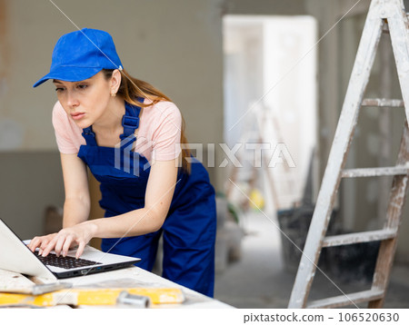 Portrait of a female builder who checks the work done using laptop Portrait of a female builder who checks the work done using laptop 106520630