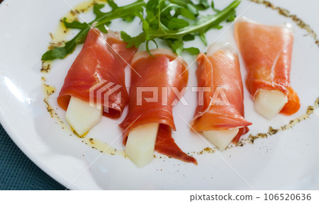 Rolls of iberian jamon stuffed with melon at plate with arugula 106520636