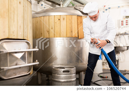 Brewmaster fixing hose pipe in workshop of beer factory 106520744