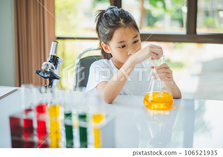 little scientist looking through a microscope and test tubes filled with chemicals for learning about science and experiments. little scientist looking through a microscope and test tubes filled with chemicals for learning about science and experiments. 106521935