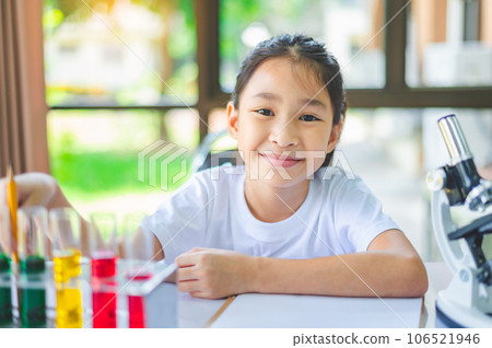 little scientist looking through a microscope and test tubes filled with chemicals for learning about science and experiments. little scientist looking through a microscope and test tubes filled with chemicals for learning about science and experiments. 106521946