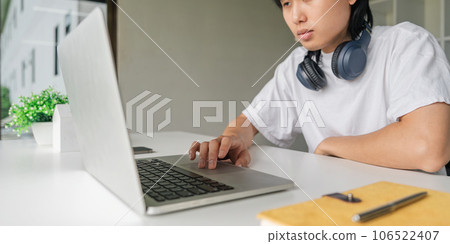 Asian young man using laptop while relax sitting at the table Asian young man using laptop while relax sitting at the table 106522407