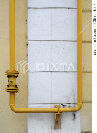 Urban still life with a yellow gas pipe and valve on the background of yellow wall with white column Urban still life with a yellow gas pipe and valve on the background of yellow wall with white column 106523639