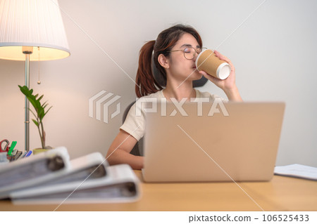 Stressed Asian woman drinking Coffee while working, female businesswoman using laptop with tired and sleepy at office, Exhausted woman with computer at home late night. Overload and Overworked Stressed Asian woman drinking Coffee while working, female businesswoman using laptop with tired and sleepy at office, Exhausted woman with computer at home late night. Overload and Overworked 106525433