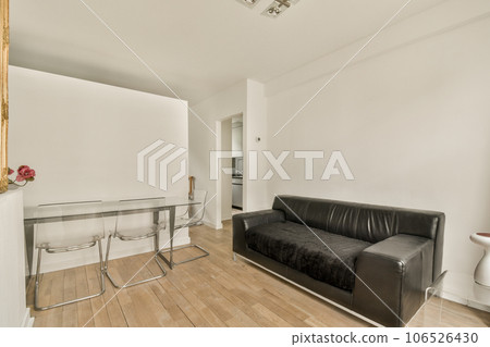 a living room with white walls and hardwood flooring, including a black leather couch in the center of the room a living room with white walls and hardwood flooring, including a black leather couch in the center of the room 106526430
