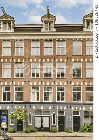 an apartment building in the middle of amsterdam, with cars parked on the street next to it and blue sky above 106526443