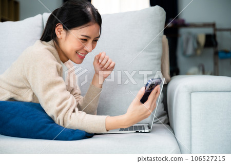 Happy young asian woman relax on comfortable couch at home texting messaging on smartphone Happy young asian woman relax on comfortable couch at home texting messaging on smartphone 106527215