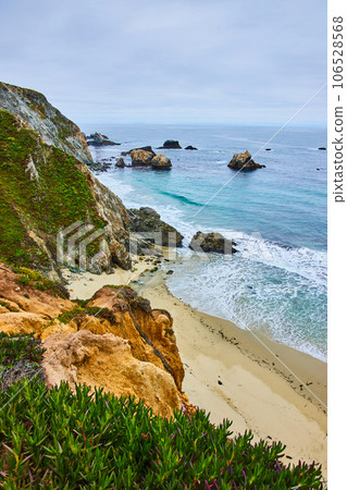 Scenic green cliffy hillside with sandy shore below and ocean waves crashing into shoreline Scenic green cliffy hillside with sandy shore below and ocean waves crashing into shoreline 106528568