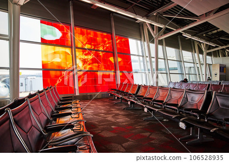 Rows of nearly empty airport terminal leather seating with abstract fiery red and orange window art 106528935