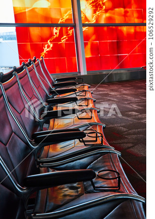 Close up of a single row of leather airport terminal seating leading to window with red abstract art 106529292