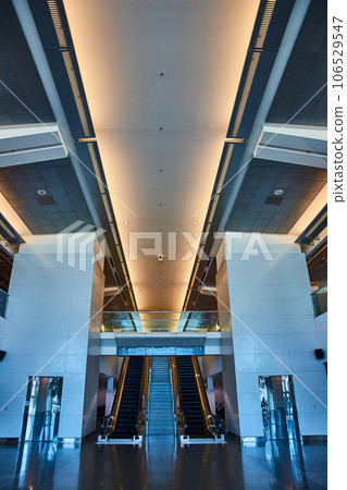 Empty symmetrical airport hallway with stairs framed by escalators and elevators leading to bridge Empty symmetrical airport hallway with stairs framed by escalators and elevators leading to bridge 106529547
