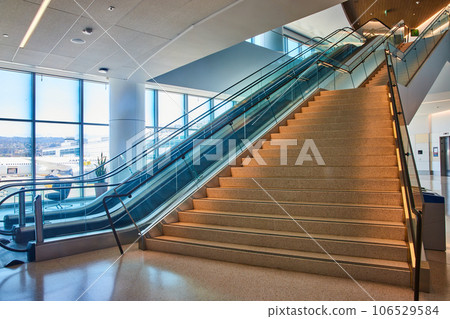 Bottom to top view of generic stairs ascending with two escalators on left side and distant elevator 106529584