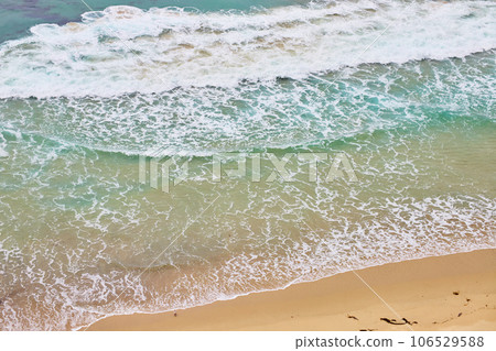 Teal ocean water with frothy waves crashing against sandy shore aerial 106529588