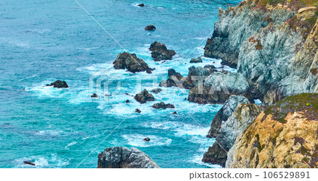 Gorgeous aerial of azure and purple Pacific Ocean crashing against yellow cliffs and dark crags Gorgeous aerial of azure and purple Pacific Ocean crashing against yellow cliffs and dark crags 106529891