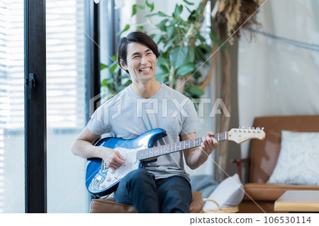 Young man practicing guitar at home 106530114