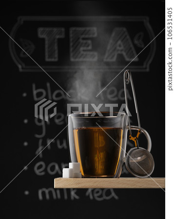 Clear glass mug with hot black tea, refined sugar and strainer against chalkboard background with tea written on it. Clear glass mug with hot black tea, refined sugar and strainer against chalkboard background with tea written on it. 106531405