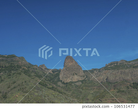 Scenic landscape with Roque de Agando rock at hiking trail through Barranco de Guarimiar Gorge. Green mountain canyon walls, blue sky background. Copy space. La Gomera, Canary Islands, Spain 106531477