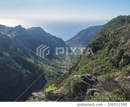 view of village El Retamal in green valley with palm trees, with terraced fields and traditional colorful houses. Valle Gran Rey, La Gomera, Canary Islands, Spain, Europe. Blue sky white clouds view of village El Retamal in green valley with palm trees, with terraced fields and traditional colorful houses. Valle Gran Rey, La Gomera, Canary Islands, Spain, Europe. Blue sky white clouds 106531500