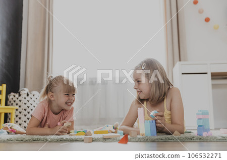 Children playing with colorful toys. Kids lying on carpet at home bedroom or kindergarten, nursery. Educational eco-friendly game for child. Creative happy preschool age sweet child 106532271