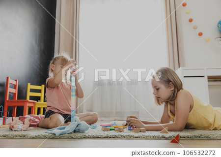 Children playing with colorful wooden toy train. Kids sitting on carpet at home bedroom, kindergarten, daycare playroom, playground, play center. Funny educational eco-friendly game for child Children playing with colorful wooden toy train. Kids sitting on carpet at home bedroom, kindergarten, daycare playroom, playground, play center. Funny educational eco-friendly game for child 106532272