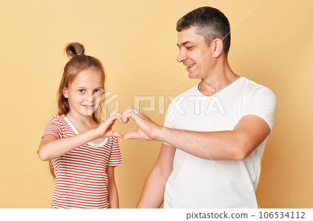 Cute smiling brwon haired little girl standing with her father and making heart shape with hands together expressing love family realtionship. Cute smiling brwon haired little girl standing with her father and making heart shape with hands together expressing love family realtionship. 106534112
