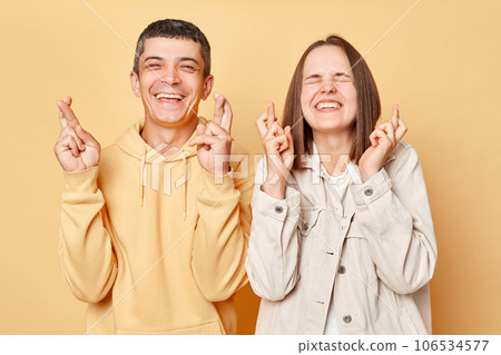 Hopeful woman and man wearing casual style clothing standing isolated over beige background making wishtogetherposing with crossed fingers dreaming for good luck. 106534577