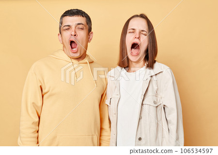 Sleepy tired friends woman and man wearing casual style clothing standing isolated over beige background yawning needs rest, drowsing, having nap. 106534597