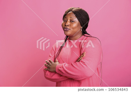 Portrait of excited friendly young adult standing with arm crossed smiling at camera during shoot time posing with confidence in studio with pink background. Cheerful woman with charming expression Portrait of excited friendly young adult standing with arm crossed smiling at camera during shoot time posing with confidence in studio with pink background. Cheerful woman with charming expression 106534843