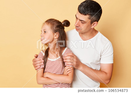 Offended daughter tunrning away from her father family wearing casual t-shirts standing isolated over beige background dad and kid arguing. 106534873