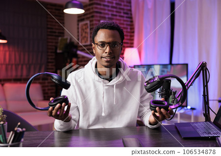 Portrait of technology vlogger comparing and reviewing over the ear headphones in living room studio. Knowledgeable content creator filming audiophiles channel vlog for streaming service Portrait of technology vlogger comparing and reviewing over the ear headphones in living room studio. Knowledgeable content creator filming audiophiles channel vlog for streaming service 106534878