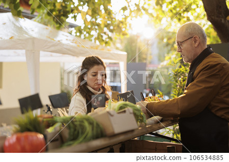 Family couple or organic farmers waiting for first customers while working at farm market. Vendors preparing produce stand while selling fresh local produce home-grown fruits and vegetables Family couple or organic farmers waiting for first customers while working at farm market. Vendors preparing produce stand while selling fresh local produce home-grown fruits and vegetables 106534885