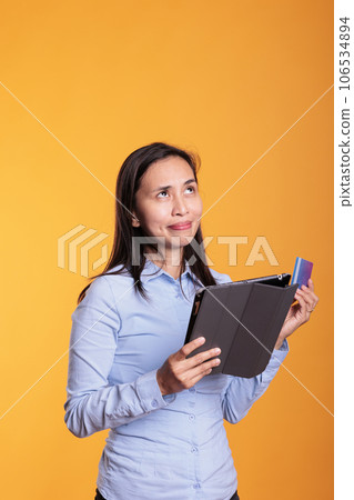 Asian woman doing online shopping holding tablet computer, typing credit card information making online purchase. Cheerfu young adult ordering fashion clothes in studio over yellow background Asian woman doing online shopping holding tablet computer, typing credit card information making online purchase. Cheerfu young adult ordering fashion clothes in studio over yellow background 106534894