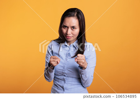 Defensive filipino fighter holding arms in self defense when encountering a life threat. Brave filipino woman clenching fists ready for boxing match, standing in studio over yellow background 106534895