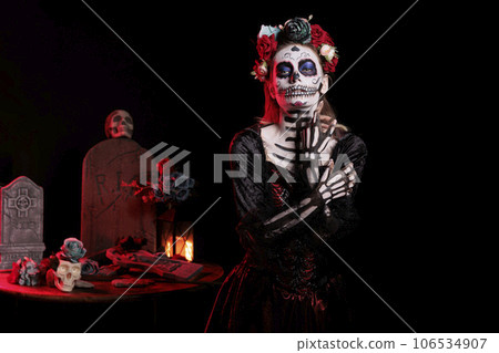 Creepy lady of death with skull make up and colorful wreath of flowers, acting like holy santa muerte on day of the dead celebration. Beautiful goddess wearing festival tradition costume. Creepy lady of death with skull make up and colorful wreath of flowers, acting like holy santa muerte on day of the dead celebration. Beautiful goddess wearing festival tradition costume. 106534907