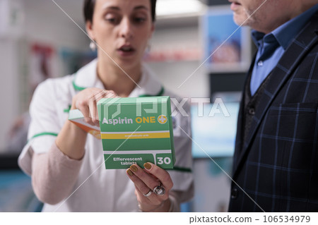 Pharmaceutical consultant holding painkiller package and explaining aspirin dosage instruction to customer in drugstore. Pharmacy employee advising man pills for inflammation treatment 106534979