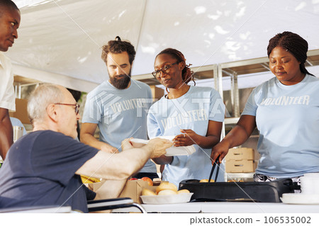 Charity group provides support and distributes free food to homeless people showcasing commitment to fight hunger and poverty. Voluntary individuals serving warm meal to caucasian wheelchair user. 106535002