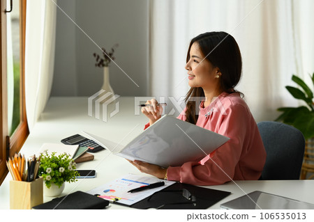 Charming millennial female manager sitting at office desk and looking away, daydreaming or thinking of new business ideas 106535013