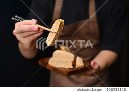 Man holding Tempeh with bamboo chopsticks Vegan appetizers, traditional Indonesian soy product Man holding Tempeh with bamboo chopsticks Vegan appetizers, traditional Indonesian soy product 106535128
